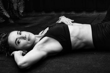 A woman in a sports bra lying on the floor in a contemplative pose.
